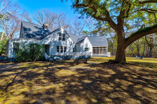 exterior space with a front yard, a sunroom, roof with shingles, and a chimney