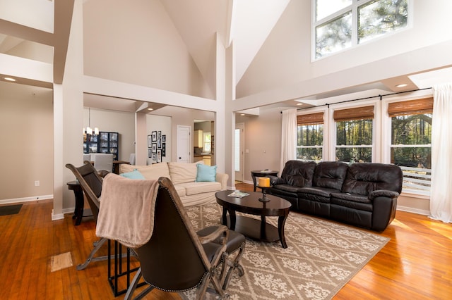 living area featuring high vaulted ceiling, wood-type flooring, baseboards, and a notable chandelier