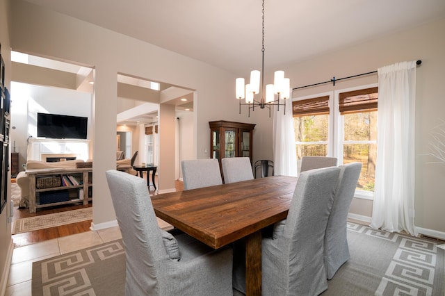 dining space featuring light tile patterned floors, a fireplace, baseboards, and a notable chandelier