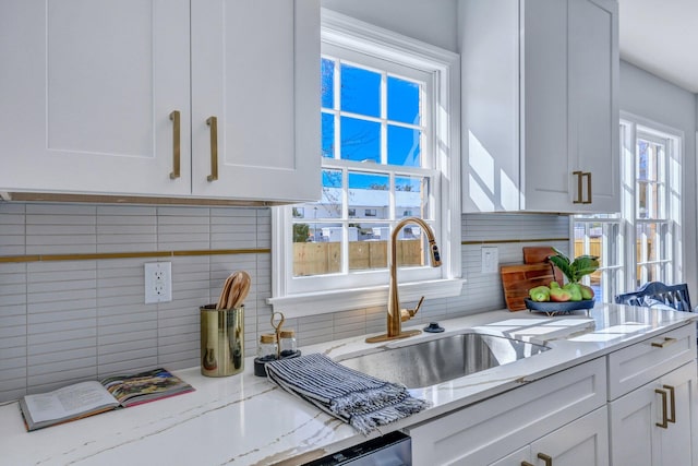 kitchen with light stone countertops, sink, and white cabinets