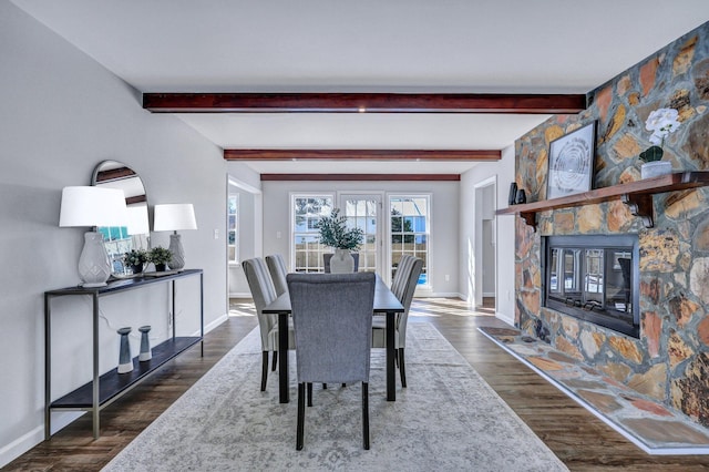 dining space featuring beamed ceiling, dark hardwood / wood-style flooring, and a stone fireplace