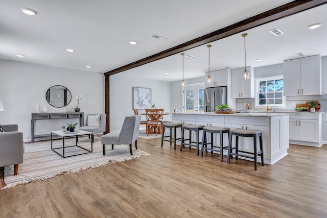 living room featuring beamed ceiling, sink, and light hardwood / wood-style flooring