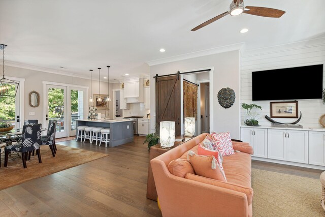 living room featuring crown molding, dark wood-type flooring, ceiling fan, and a barn door