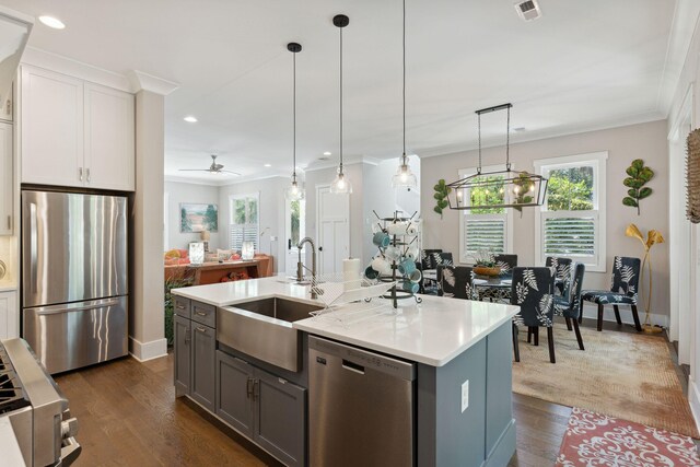 kitchen featuring pendant lighting, ceiling fan with notable chandelier, stainless steel appliances, an island with sink, and dark hardwood / wood-style floors