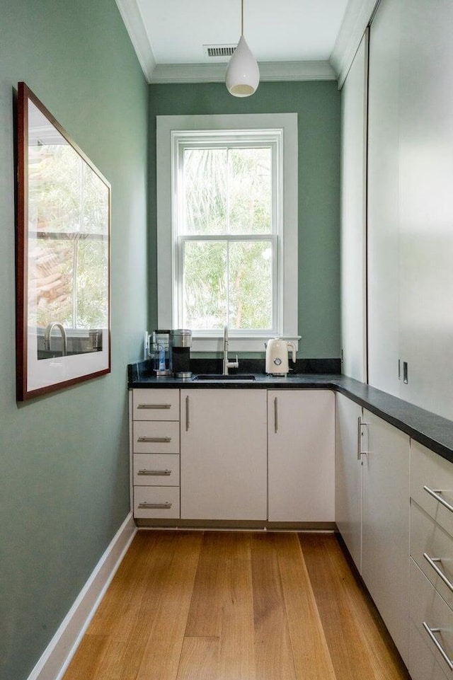 222 Haddrell St, Mount Pleasant, SC 29464 - kitchen featuring a sink, light wood finished floors, dark countertops, hanging light fixtures, and crown molding