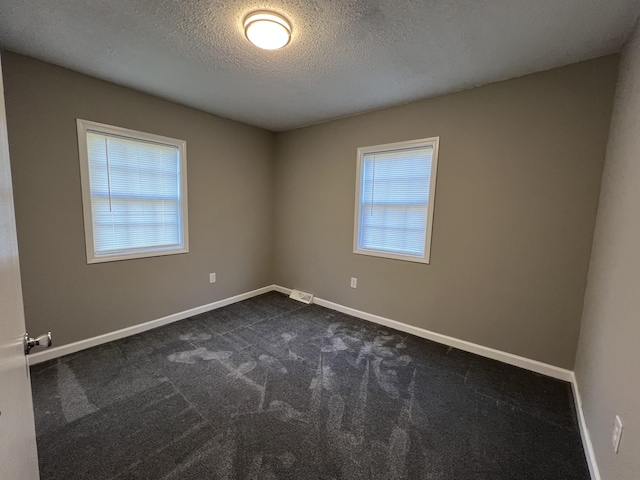 empty room with a textured ceiling and dark colored carpet