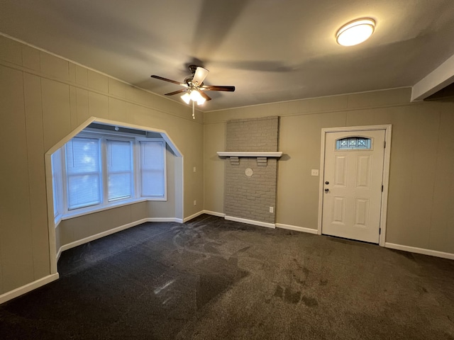 entryway with ceiling fan, a fireplace, and dark carpet