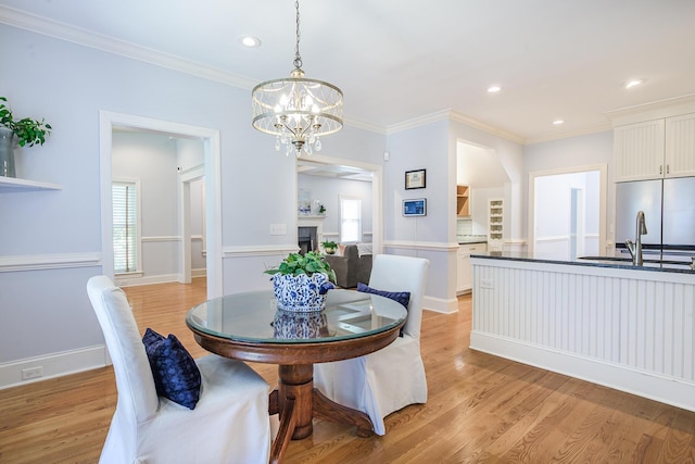 dining space featuring crown molding, recessed lighting, an inviting chandelier, light wood-type flooring, and a fireplace
