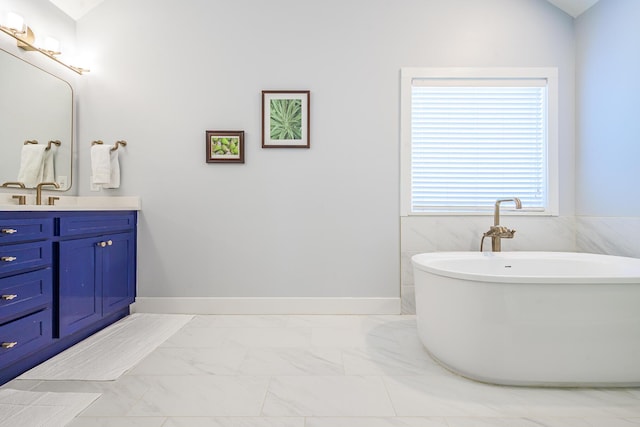 bathroom featuring marble finish floor, vanity, baseboards, and a freestanding bath