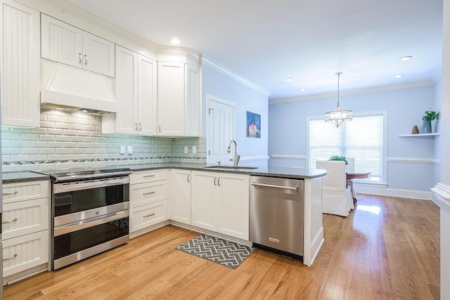 kitchen featuring a peninsula, ornamental molding, stainless steel appliances, premium range hood, and a sink