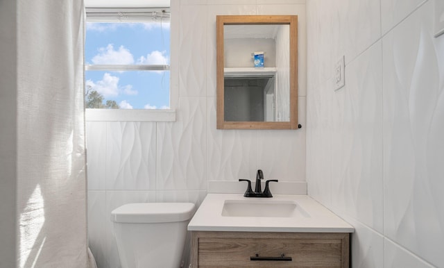 bathroom with toilet, vanity, and tile walls