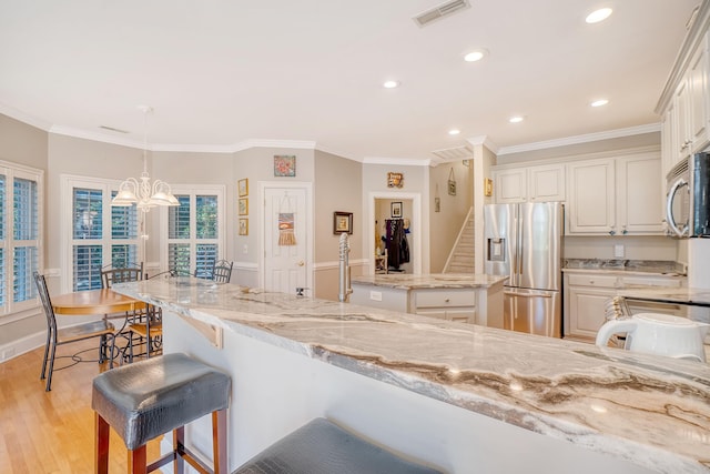 kitchen featuring pendant lighting, light stone countertops, light wood-type flooring, ornamental molding, and stainless steel appliances