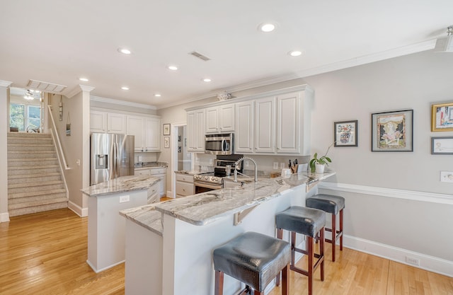 kitchen with kitchen peninsula, appliances with stainless steel finishes, light hardwood / wood-style flooring, white cabinets, and a center island