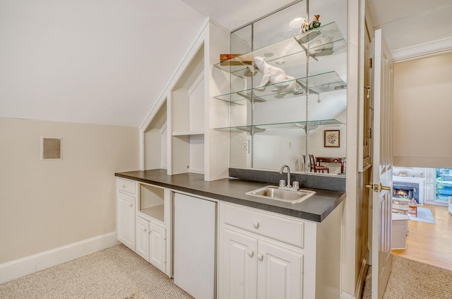 kitchen with lofted ceiling, white cabinetry, sink, and light carpet