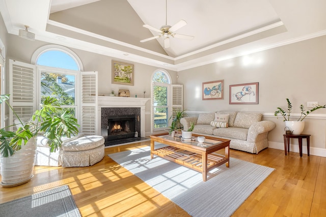 living room with ceiling fan, light hardwood / wood-style flooring, a high end fireplace, crown molding, and a tray ceiling