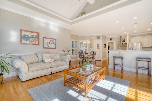 living room featuring light wood-type flooring, an inviting chandelier, vaulted ceiling, and ornamental molding