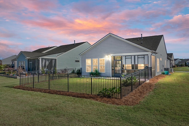 back house at dusk featuring a sunroom, a yard, and central AC unit