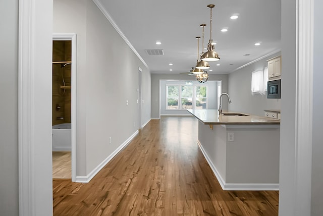 kitchen with stainless steel microwave, sink, hanging light fixtures, light hardwood / wood-style flooring, and crown molding