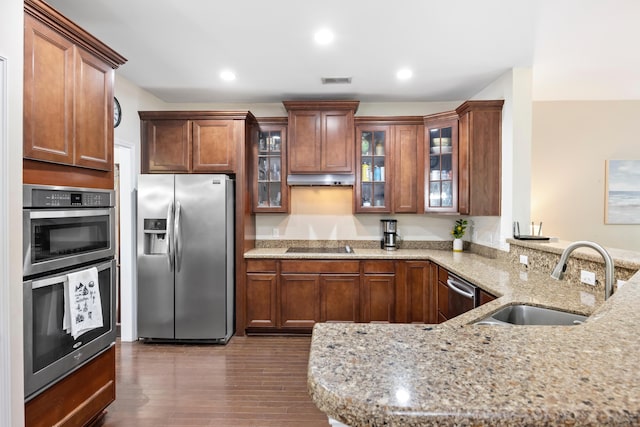 kitchen featuring appliances with stainless steel finishes, a sink, a peninsula, light stone counters, and dark wood-type flooring