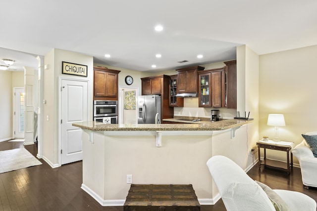 kitchen featuring stainless steel appliances, a peninsula, a breakfast bar area, dark wood-style flooring, and glass insert cabinets