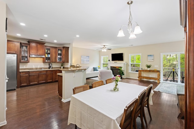 dining room featuring a fireplace, ceiling fan, dark wood-type flooring, a chandelier, and recessed lighting