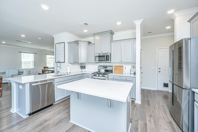 kitchen featuring ornamental molding, a peninsula, gray cabinets, a sink, and appliances with stainless steel finishes