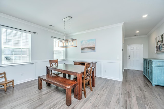 dining space with ornamental molding, light wood-style flooring, and a wainscoted wall
