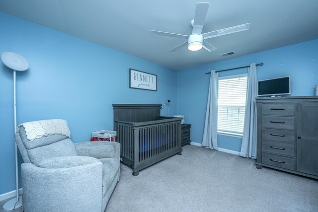 bedroom with visible vents, light carpet, baseboards, a nursery area, and a ceiling fan