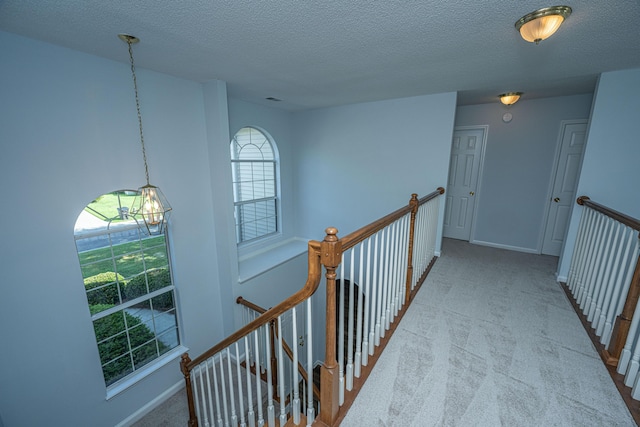 hallway with light colored carpet and a textured ceiling