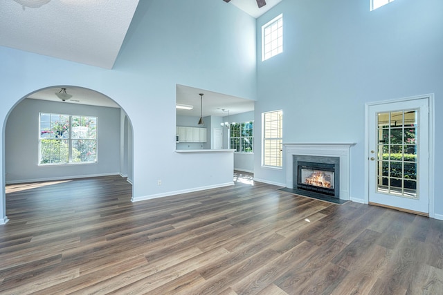 unfurnished living room featuring a premium fireplace, a towering ceiling, an inviting chandelier, and dark hardwood / wood-style flooring