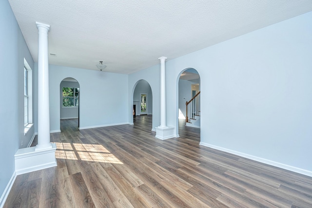 empty room with ornate columns, a textured ceiling, and dark hardwood / wood-style flooring