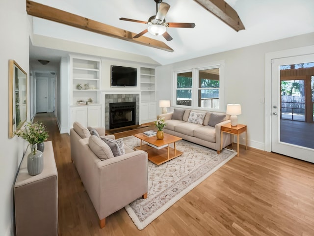 living room with ceiling fan, beam ceiling, a tile fireplace, and hardwood / wood-style floors