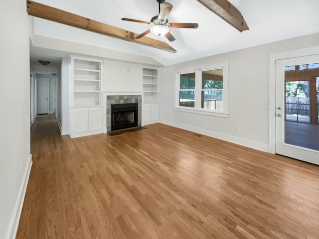 unfurnished living room with light hardwood / wood-style floors, a tiled fireplace, beamed ceiling, and ceiling fan