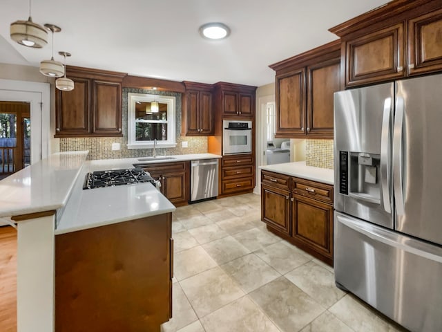 kitchen with appliances with stainless steel finishes, independent washer and dryer, a center island, sink, and decorative light fixtures