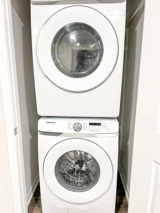 washroom with stacked washing maching and dryer and dark wood-type flooring