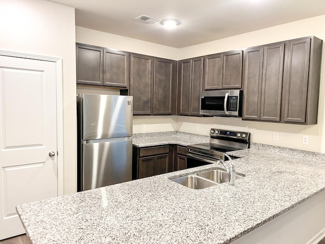 kitchen featuring light stone counters, kitchen peninsula, sink, stainless steel appliances, and dark brown cabinetry