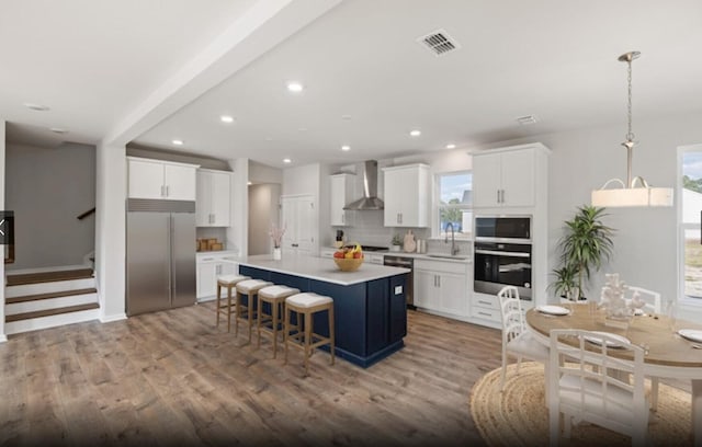 kitchen featuring a kitchen island, appliances with stainless steel finishes, wall chimney range hood, and white cabinetry