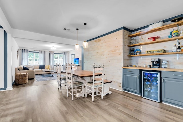 dining area with beverage cooler, light hardwood / wood-style flooring, indoor bar, and wooden walls