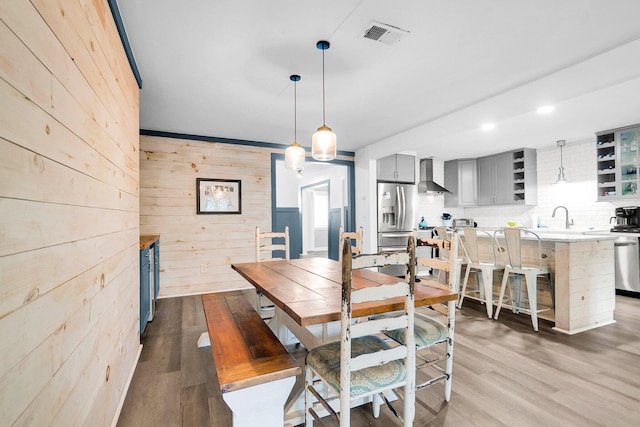 dining area with light wood-type flooring, wooden walls, and sink