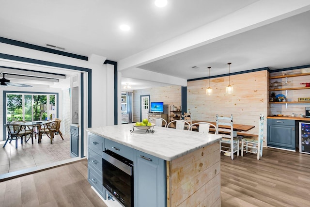 kitchen with pendant lighting, beverage cooler, a kitchen island, wood walls, and light hardwood / wood-style flooring