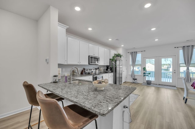 kitchen with white cabinetry, sink, stainless steel appliances, kitchen peninsula, and light hardwood / wood-style floors