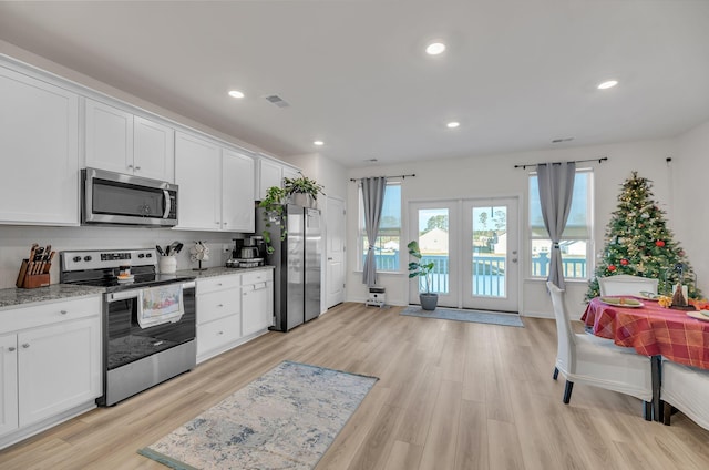 kitchen featuring white cabinets, light wood-type flooring, appliances with stainless steel finishes, tasteful backsplash, and light stone counters