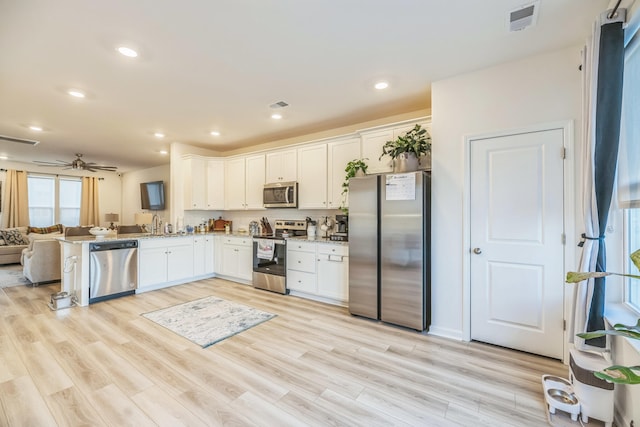 kitchen with kitchen peninsula, light hardwood / wood-style flooring, white cabinets, and appliances with stainless steel finishes