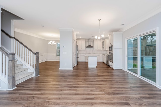 kitchen with pendant lighting, appliances with stainless steel finishes, white cabinetry, a chandelier, and wall chimney exhaust hood