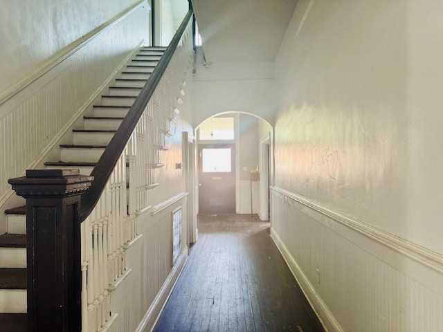 hallway with arched walkways, hardwood / wood-style flooring, a wainscoted wall, and stairs