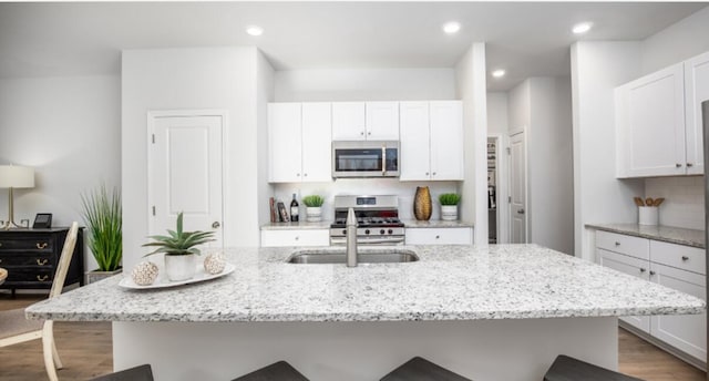 kitchen with appliances with stainless steel finishes, an island with sink, light stone countertops, and white cabinets