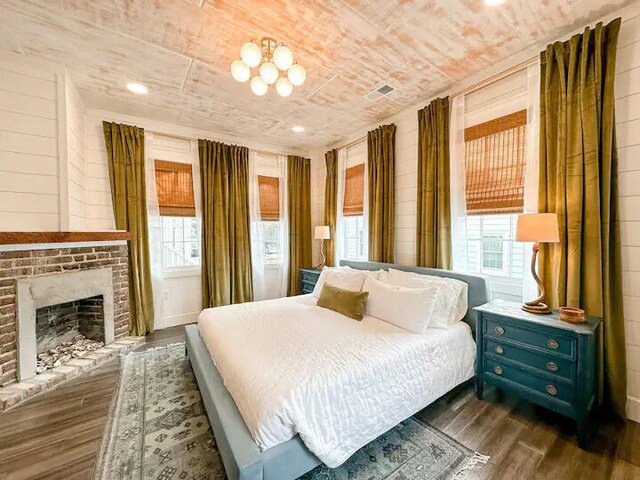 bedroom with a brick fireplace and dark wood-type flooring