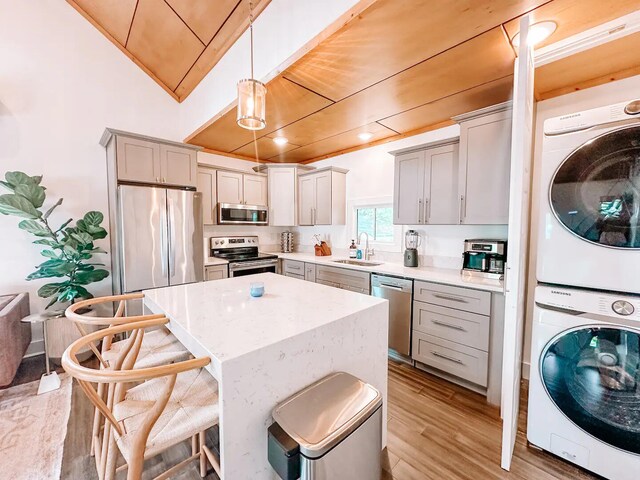 kitchen featuring stacked washer / dryer, appliances with stainless steel finishes, a kitchen island, sink, and hanging light fixtures