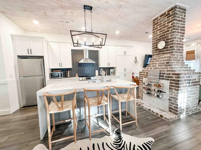 kitchen with wall chimney range hood, a center island with sink, a breakfast bar, white cabinetry, and appliances with stainless steel finishes