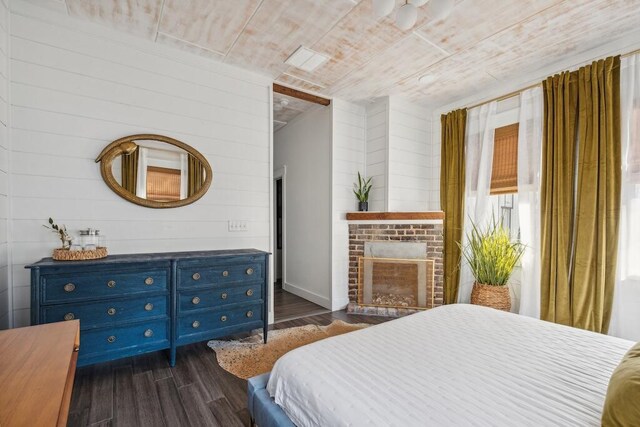 bedroom featuring dark hardwood / wood-style flooring, wood walls, and a fireplace